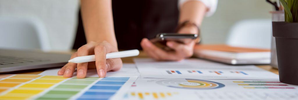 Businesswoman standing and holding digital pen, smartphone with working on laptop in the office.